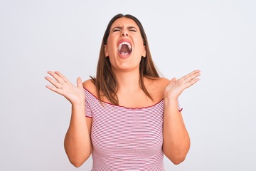 Fototapeta na wymiar Portrait of beautiful young woman standing over isolated white background crazy and mad shouting and yelling with aggressive expression and arms raised. Frustration concept.