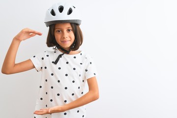 Beautiful child girl wearing security bike helmet standing over isolated white background gesturing with hands showing big and large size sign, measure symbol. Smiling looking at the camera