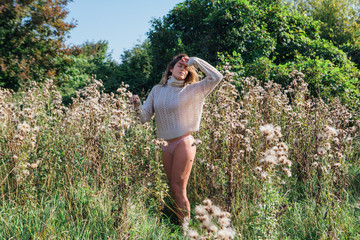 Happy young beautiful woman in sweater and underpants walking with bare foot in a field of dry agrimony