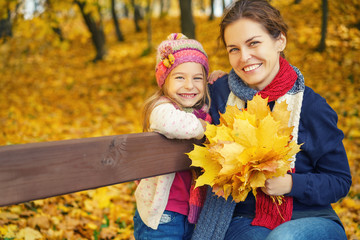 Happy little girl and her mother have fun sitting on the bench in autumn park