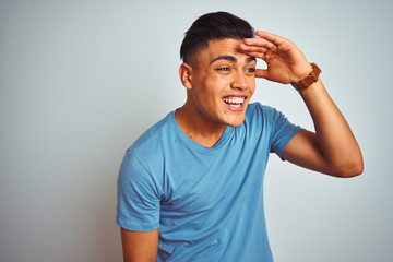 Young brazilian man wearing blue t-shirt standing over isolated white background very happy and smiling looking far away with hand over head. Searching concept.