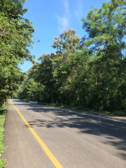 Beautiful local asphalt road way to the natural in rainy season with trees forest, blue sky and mountains in the backgrounds in the north of Thailand.