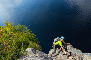 Rock climber with a rope climbing above a deep blue lake