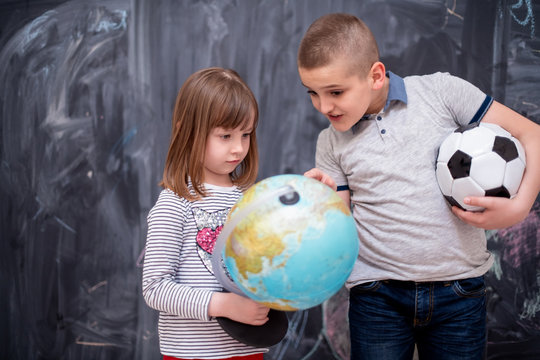 boy and little girl using globe of earth in front of chalkboard