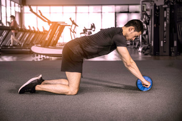 Young sportsman is doing ab wheel rollout exercise working out at fitness gym