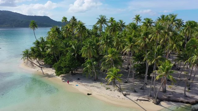 Tropical island paradise - Aerial drone video from French Polynesia of Motu Mahaea, Tahaa, Tahiti. Aerial view of atoll with palm trees, turquoise water in coral reef lagoon. Beautiful woman on beach.