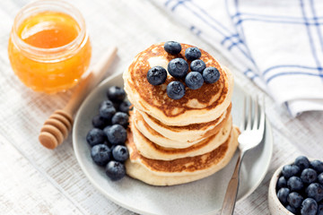 Pancakes with blueberries and honey on white wooden table. Stack of fluffy american buttermilk pancakes. Tasty breakfast