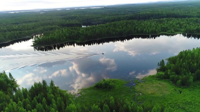 Northern river aerial scenes. Fishing boat sails on the river. Large wide river with islands covered with coniferous and mixed forests. Early morning, sun rises, clouds in the sky