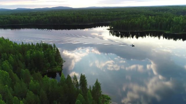 Northern river aerial scenes. Fishing boat sails on the river. Large wide river with islands covered with coniferous and mixed forests. Early morning, sun rises, clouds in the sky