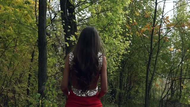Girl in a red dress riding a horse in the forest. Autumn weather and nature around. Like in the old days of the 18th century.