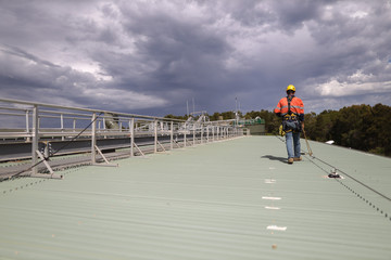 Construction safety inspector wearing fall safety harness walking on the roof by clipping safety...