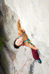 Asian woman rock clikmber holding onto nothing on a rock climbing wall outdoors, trying really hard with a grimace on her face.