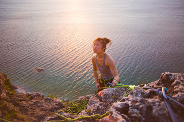 Girl climbing to the top of a seaside cliff with the sun setting behind her
