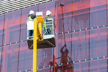 Naklejka premium workers wash windows in a tall building on a faucet. Workers Clean the Windows on Skyscraper