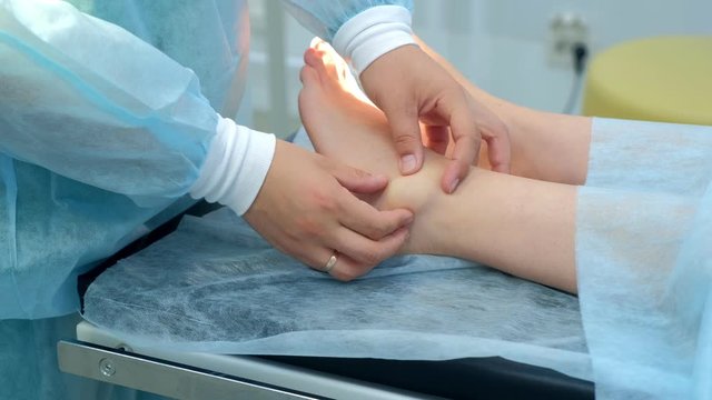 Surgeon palpates leg before surgery to remove ankle hygroma in joint, hands closeup. One day surgery concept. Examination before operation. Woman patient in hospital with doctor.