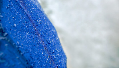 Wide screen of raindrops on blue umbrella with blurry of road on rainy day.