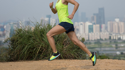 Female ultramarathon runner running on mountains next to modern city