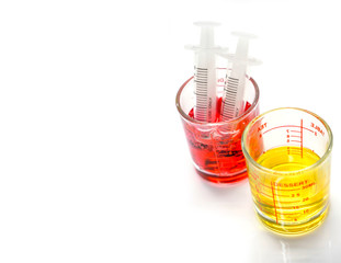 Red and yellow liquid medicine in medicine measuring glass cup with plastic syringes for ready to enter the patient mouth isolate on white background and make with paths.