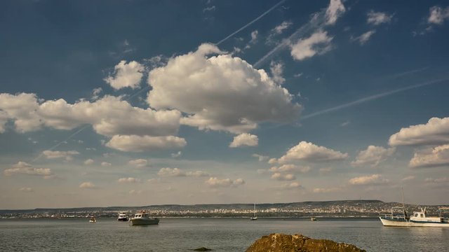 Time interval. 4k. White clouds over the sea. On the horizon a coastal city. Pleasure boats on the roadstead.