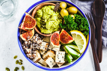 Buddha bowl with quinoa, tofu, kale, fig and guacamole hummus in a white plate, top view.