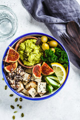 Buddha bowl with quinoa, tofu, kale, fig and guacamole hummus in a white plate, top view.