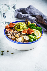 Buddha bowl with quinoa, tofu, kale, fig and guacamole hummus in a white plate.