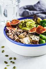 Buddha bowl with quinoa, tofu, kale, fig and guacamole hummus in a white plate.
