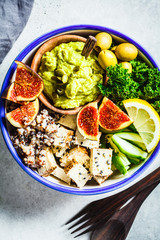 Buddha bowl with quinoa, tofu, kale, fig and guacamole hummus in a white plate, top view.