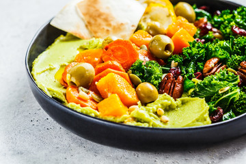 Avocado hummus with baked vegetables, olives, nuts and berries in black plate. Healthy vegan food concept.