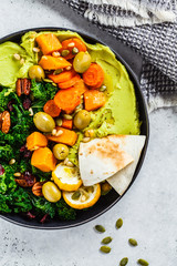 Avocado hummus with baked vegetables, olives, nuts and berries in black plate, top view. Healthy vegan food concept.