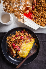 Baked oatmeal with berries and mango in black plate, top view. Homemade granola (crumble pie) with milk and fruit.