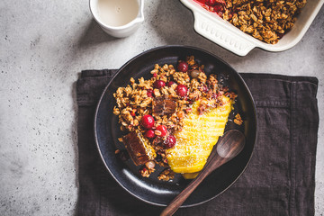 Baked oatmeal with berries and mango in black plate, top view. Homemade granola (crumble pie) with milk and fruit.