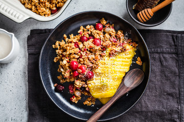 Baked oatmeal with berries and mango in black plate, top view. Homemade granola (crumble pie) with milk and fruit.