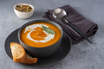 Pumpkin soup with cream on grey stone background. Copy space.