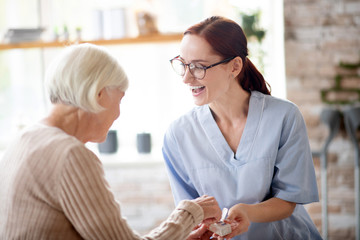 Pleasant nurse laughing while speaking with retired lady - obrazy, fototapety, plakaty