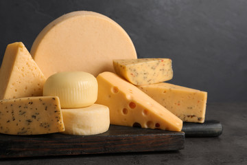 Wooden board with different sorts of cheese on grey table