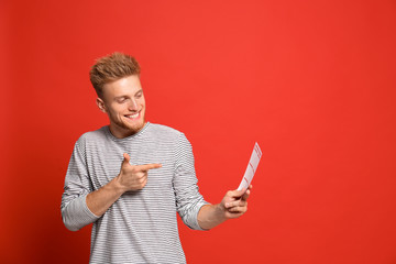 Portrait of happy young man with lottery ticket on red background