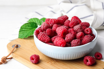 Bowl with delicious ripe raspberries on wooden cutting board, space for text