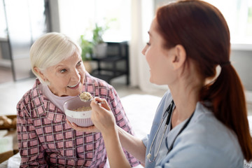 Caring nurse feeding aged woman in the morning