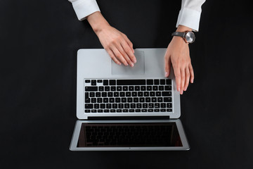 Fototapeta na wymiar Young woman using laptop on black background, top view