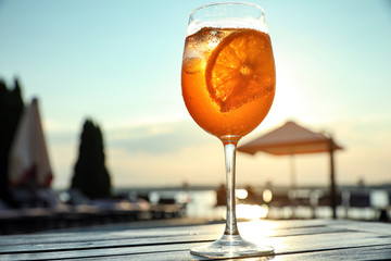 Glass of fresh summer cocktail on wooden table outdoors at sunset, low angle view