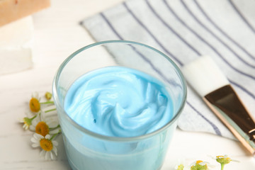 Professional face mask with flowers and brush on white wooden table, closeup
