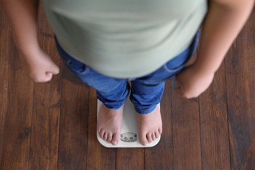 Overweight boy standing on floor scales indoors, above view - obrazy, fototapety, plakaty
