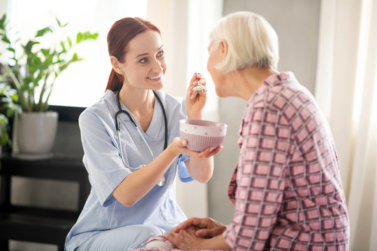 Grey-haired woman eating oatmeal and talking to nurse