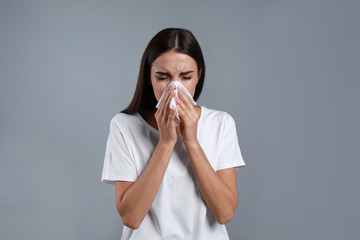 Young woman suffering from allergy on grey background