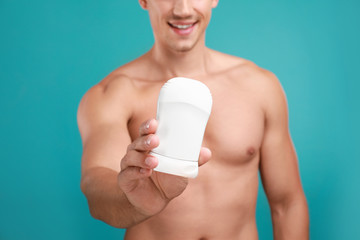 Young man with deodorant on light blue background, closeup
