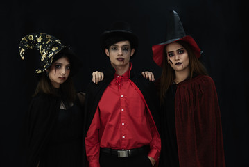 Obraz premium Three Asian people model dressed as Dracula and witch and a witch's hat costume smile and acting on Halloween party standing with a dark background.