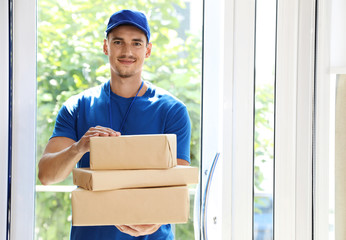Happy young courier with pile of parcels in doorway. Space for text
