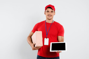 Happy young courier with tablet and parcel on white background