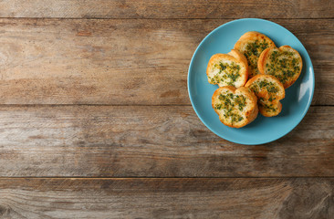 Slices of toasted bread with garlic and herbs on wooden table, top view. Space for text
